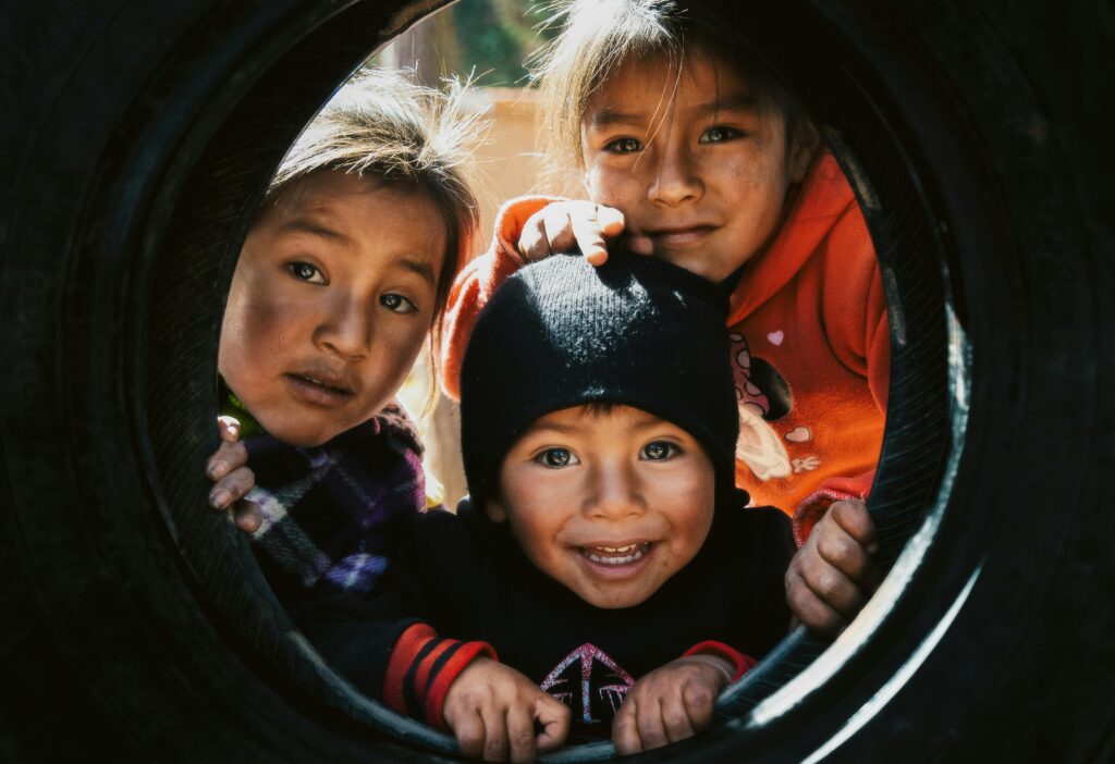 Three happy children play inside a tire swing outdoors in Cusco, Peru showcasing joy and friendship.